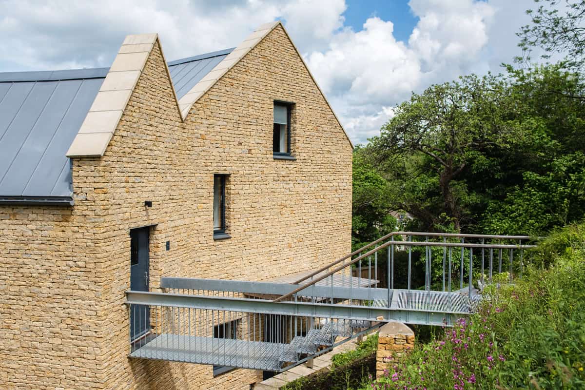 Harleywood House contemporary Cotswold stone home with twin gables, zinc roof, and metal walkway bridge